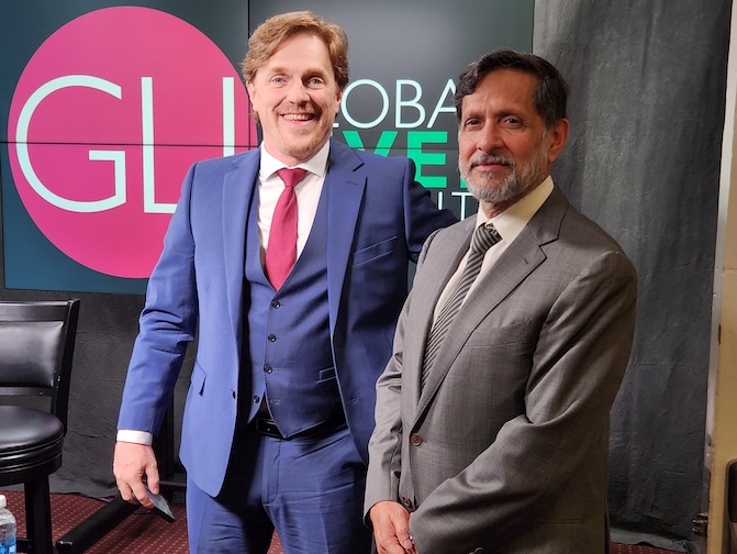Two men standing in suits in front of a Global Liver Institute sign.