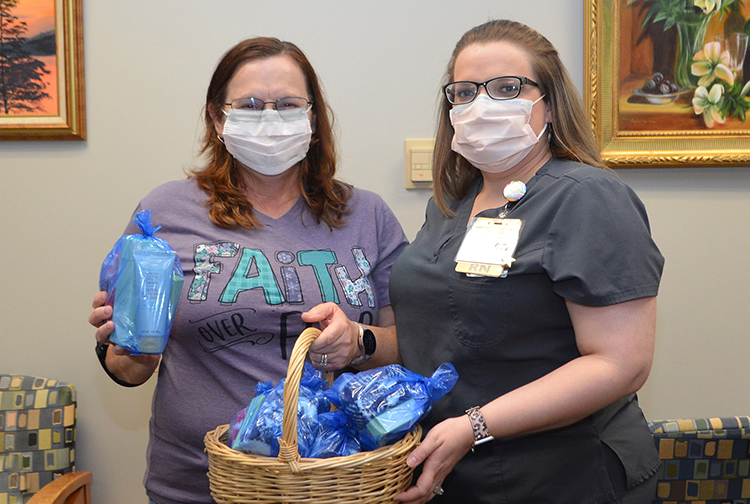 two ladies hold a basked full of bags with socks, lotion, hydrating mask and lip balm